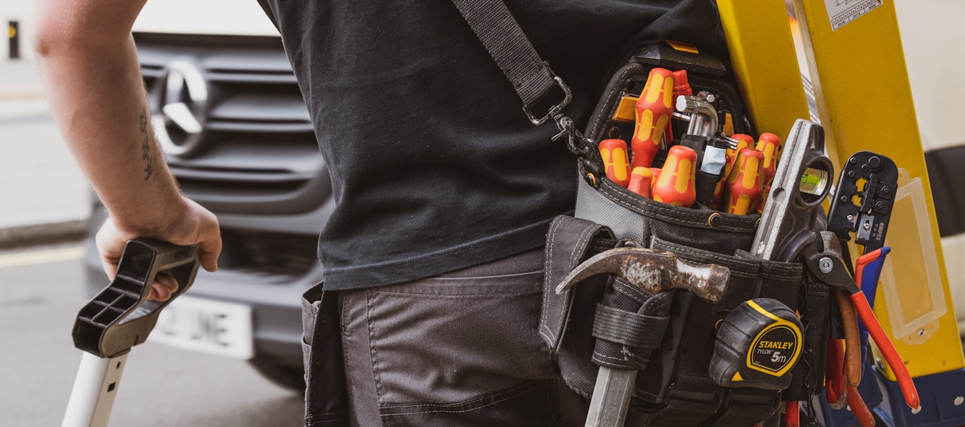 Service technician with a loaded tool belt beside a work van